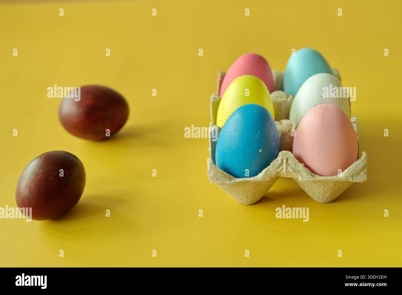 Bunte Ostereier im Karton auf gelbem Hintergrund Stockfoto