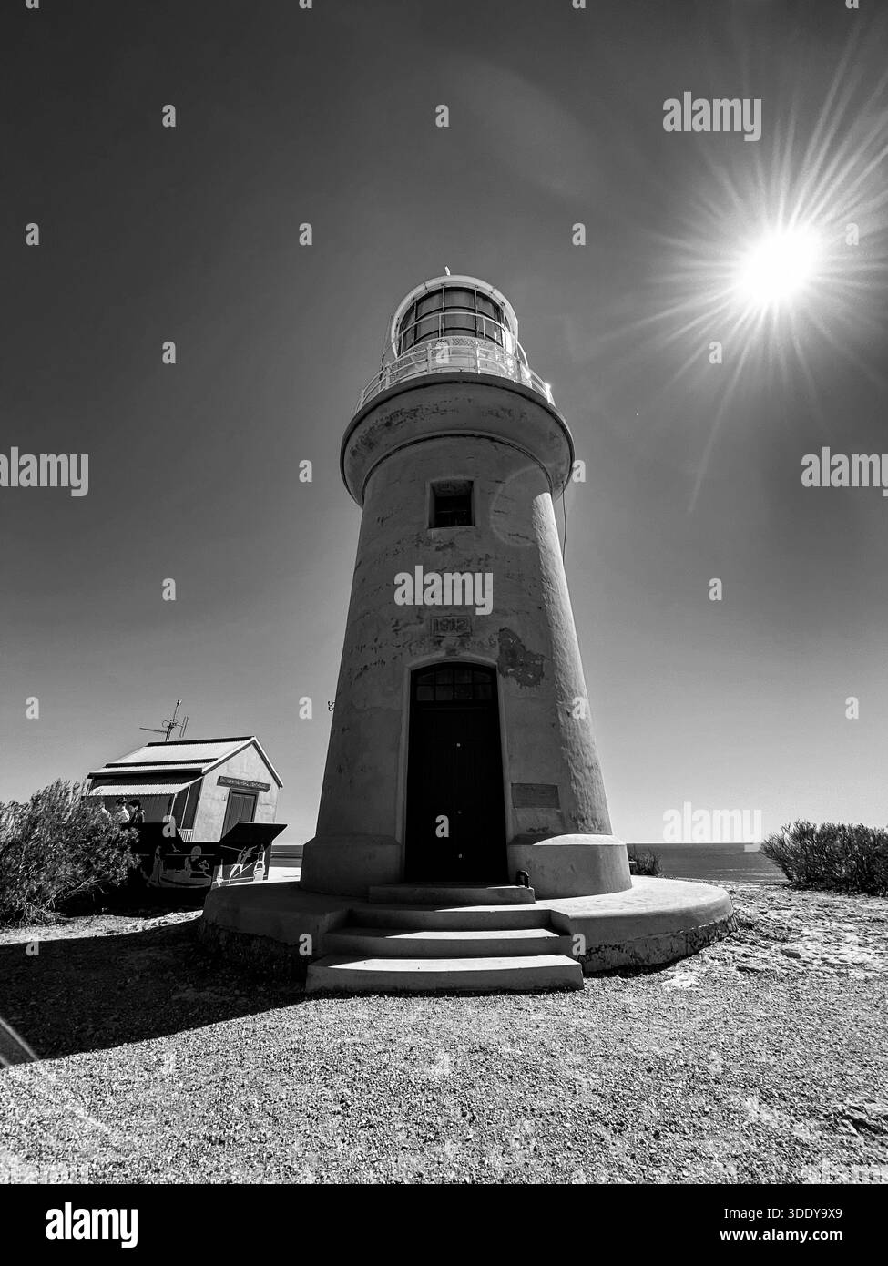 Ein einsamer Leuchtturm steht hoch vor einem hellen, sonnendurchfluteten Himmel und bietet Widerstandsfähigkeit und Führung. Stockfoto