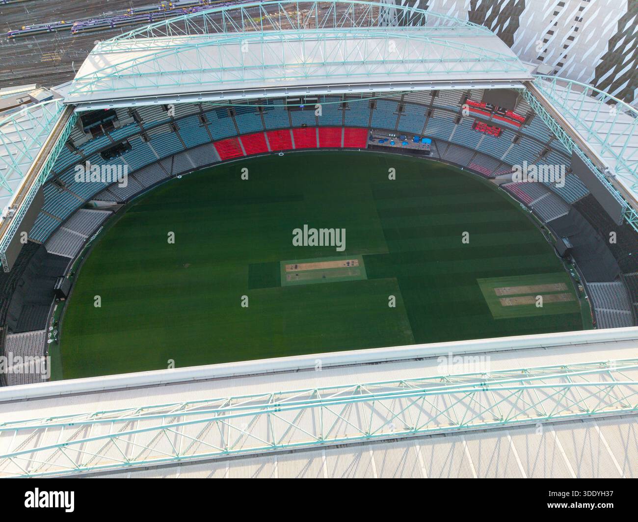 Die Luftaufnahme zeigt ein leeres Multisport-Stadion mit seinem lebhaften grünen Spielfeld, den Reihen farbiger Sitze und dem angrenzenden Eisenbahnnetz. Stockfoto