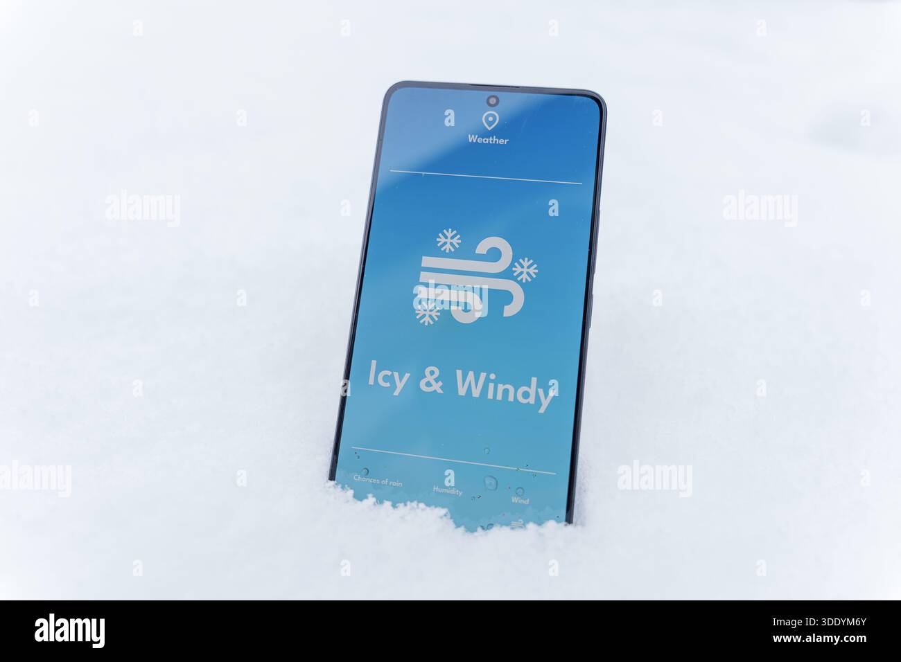Smartphone steht im Schnee mit eiskalter und windiger Wettervorhersage auf dem Bildschirm, Wintersturmkonzept. Hochwertige Fotos Stockfoto