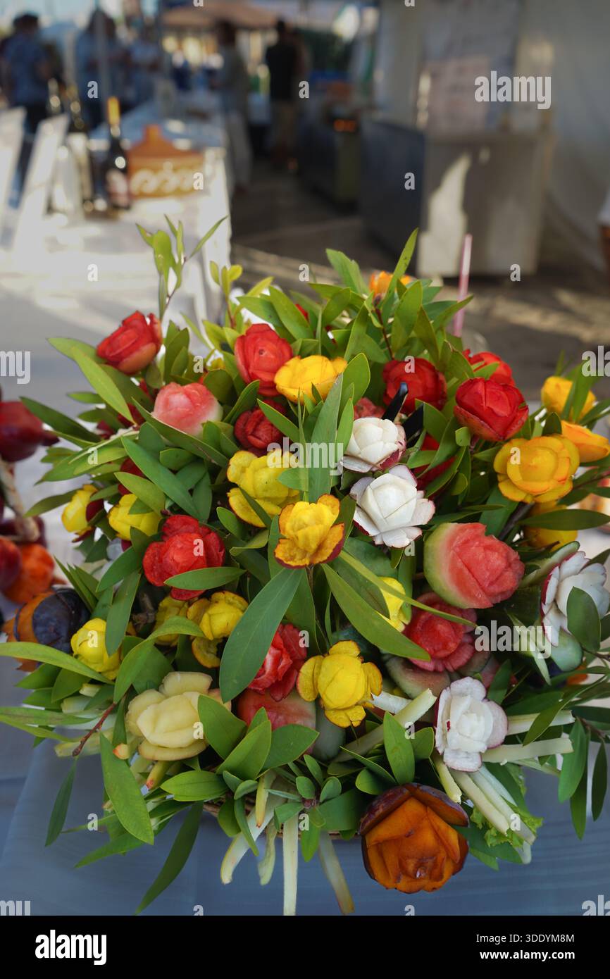 Ein kreatives und farbenfrohes Arrangement mit kunstvoll geschnitztem Obst und Gemüse in Form von Rosen und Blüten. Stockfoto