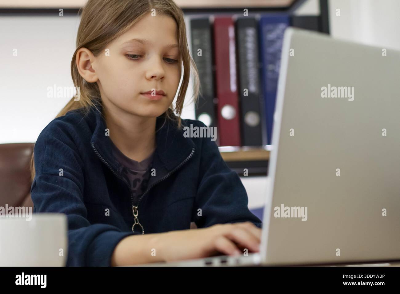 Enge Aufnahme von Gesicht und Händen des Jugendlichen Mädchens auf der Tastatur, mit verschwommenen Ordnern und Tasse im Büro. Stockfoto