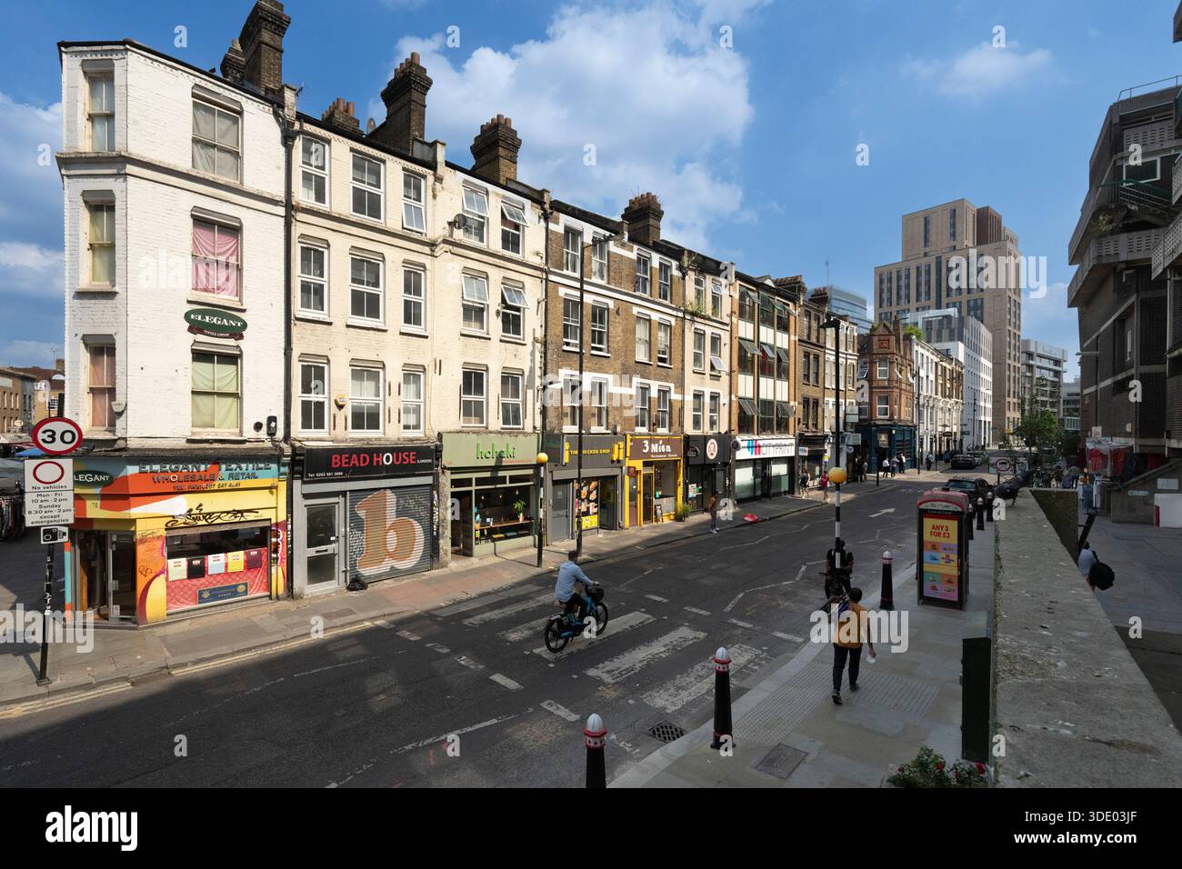 An einem sonnigen Tag überquert ein Radfahrer die Straße vor den Geschäften in der Middlesex Street Aldgate, London. Stockfoto