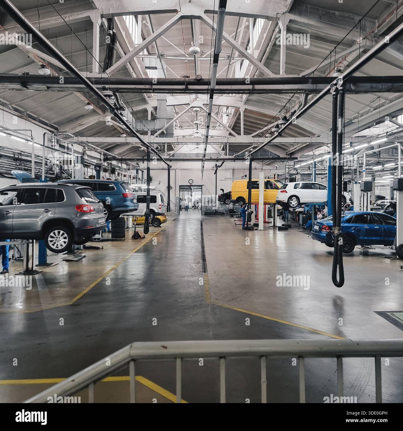 Innenraum einer großen Autowerkstatt. Eine Weitwinkelaufnahme einer geräumigen, gut beleuchteten Kfz-Tankstelle mit mehreren Fahrzeugen auf hydraulischen Hebebühnen. Stockfoto