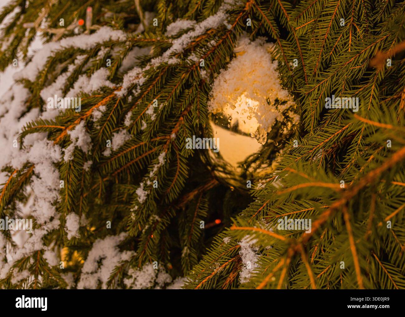 Weihnachtsbaum, dekoriert mit großen Weihnachtskugeln in Nahaufnahme. Festliche Winterstraße mit schneebedeckten Gebäuden und glühender Weihnachtsdekoration. Stockfoto