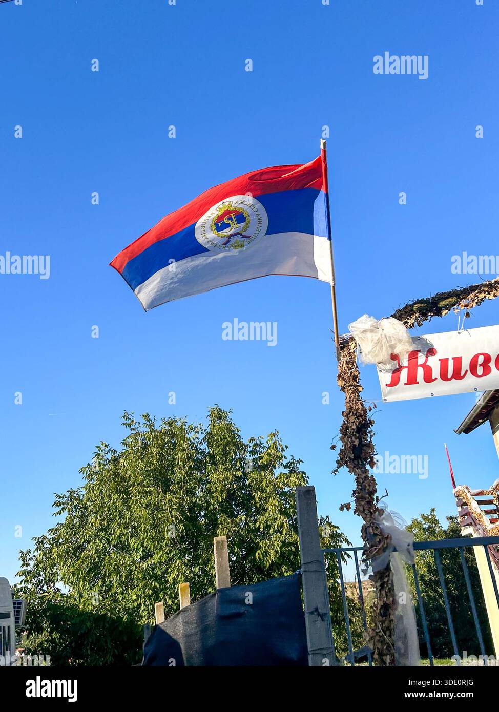 Die Flagge der Republika Srpska winkt auf einem Pfosten unter einem klaren blauen Himmel, im Tageslicht gefangen und symbolisiert die serbische Identität. Stockfoto
