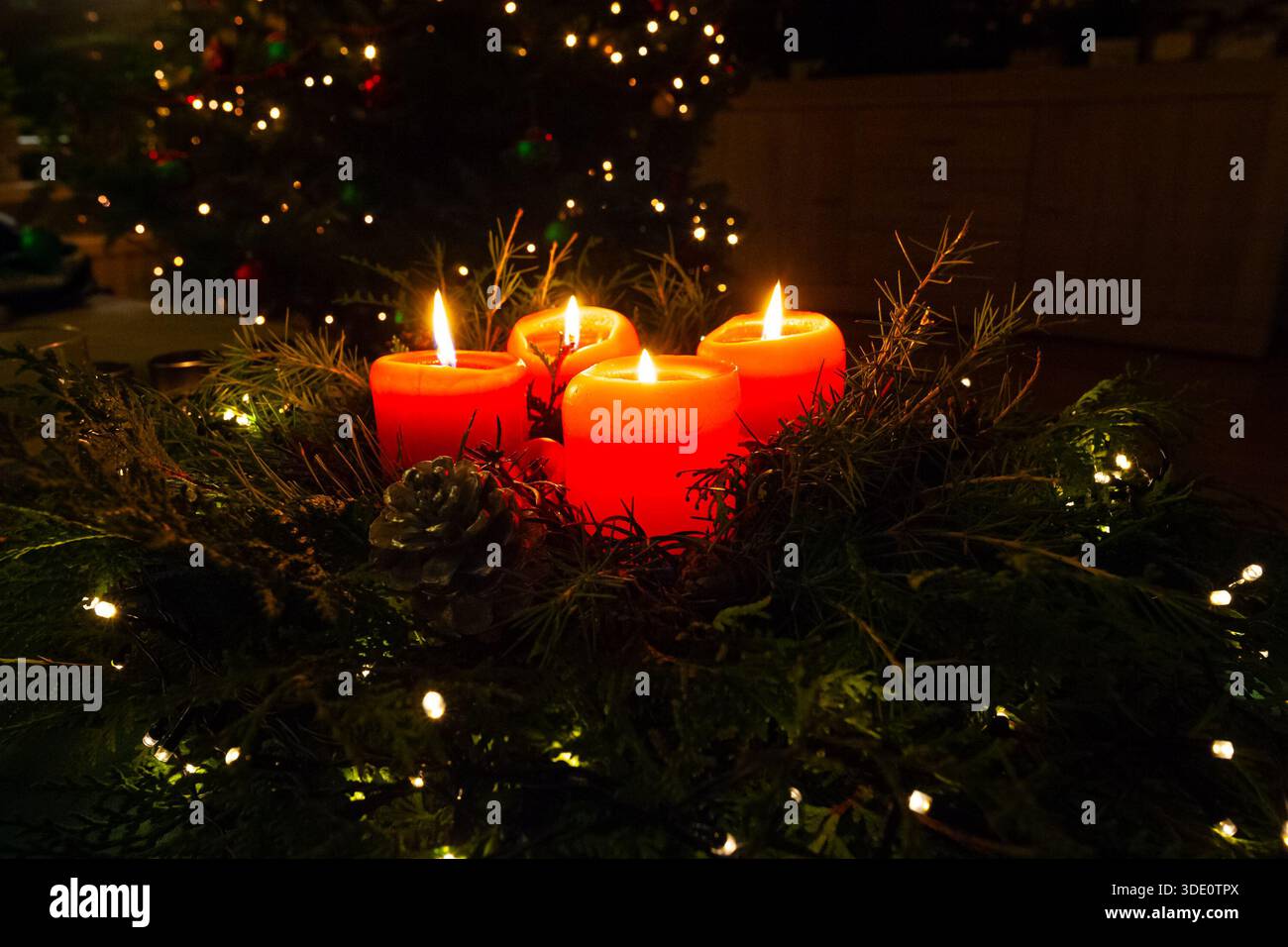 Brennende rote Adventskerzen mit weihnachtslichtern Stockfoto