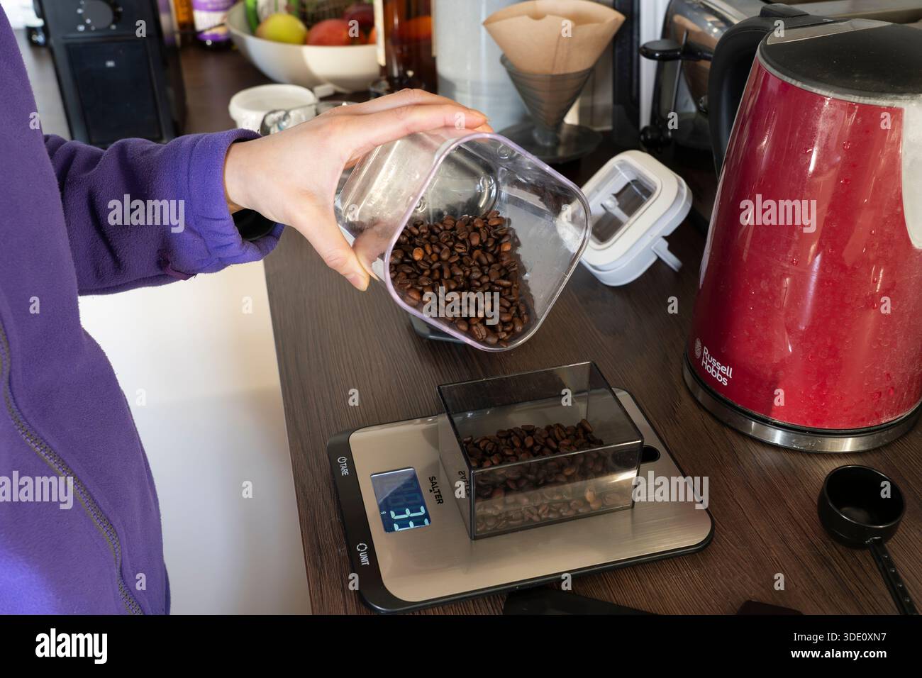 Millennial Frau, die Kaffeebohnen auf einer Waage zum Mahlen für die Kaffeezubereitung misst, Großbritannien. Konzept: Verbesserte Energie, Kaffeeabhängigkeit Stockfoto