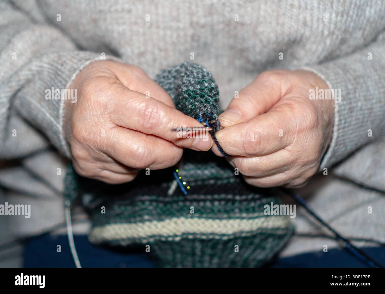 Nahaufnahme älterer Frauenhände, die mit Nadeln und grünem Wollgarn stricken. Stockfoto