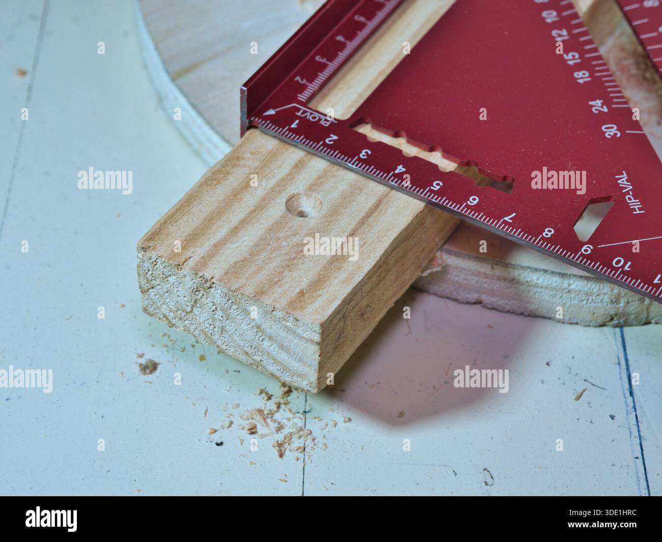 Messung von Holzdielen mit Red Speed Square Tool; Nahaufnahme eines roten Metall Speed Square Quadrats, das unbehandeltes Holz auf einer Werkbank misst. Unverzichtbares Werkzeug für DI Stockfoto