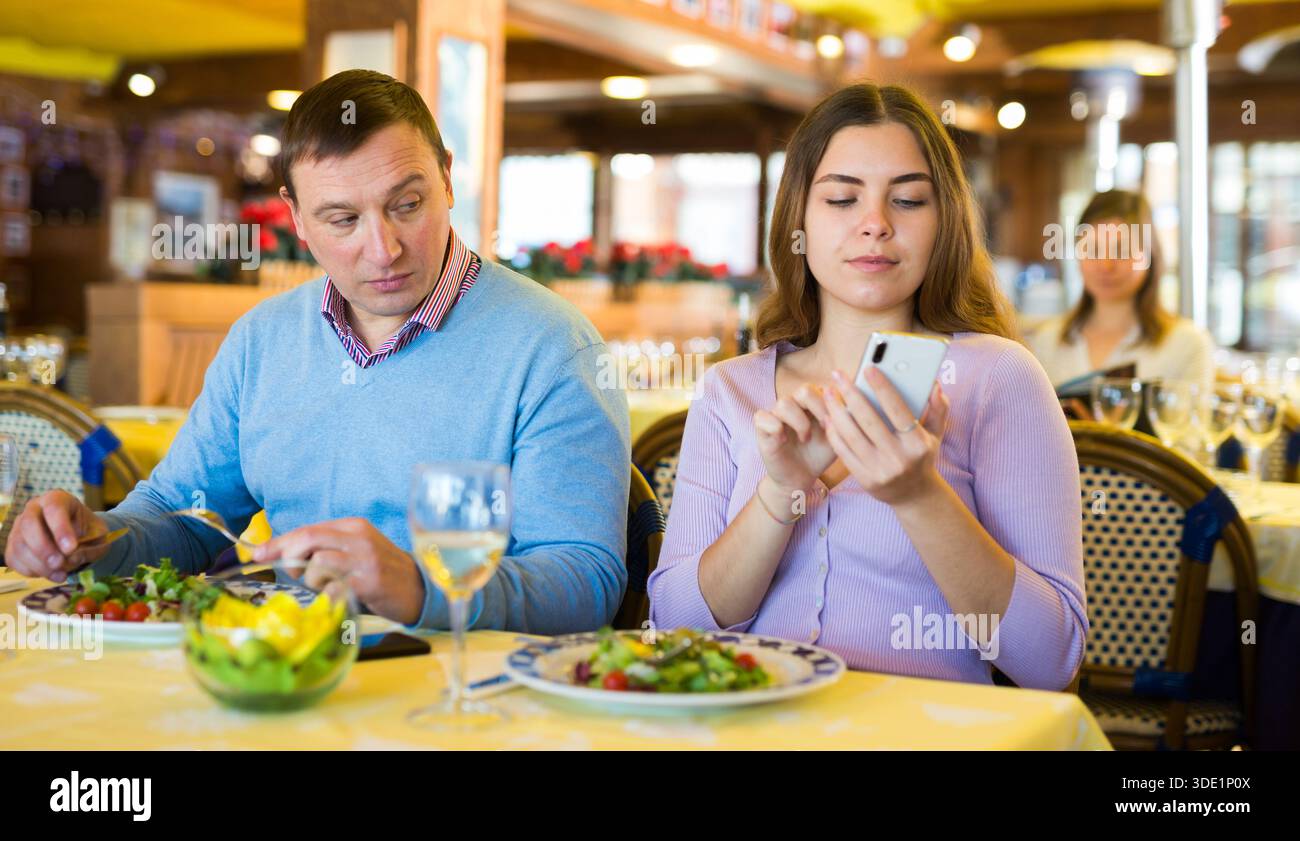 Modernes Paar, das während des Mittagessens im Restaurant Mobiltelefone benutzt Stockfoto