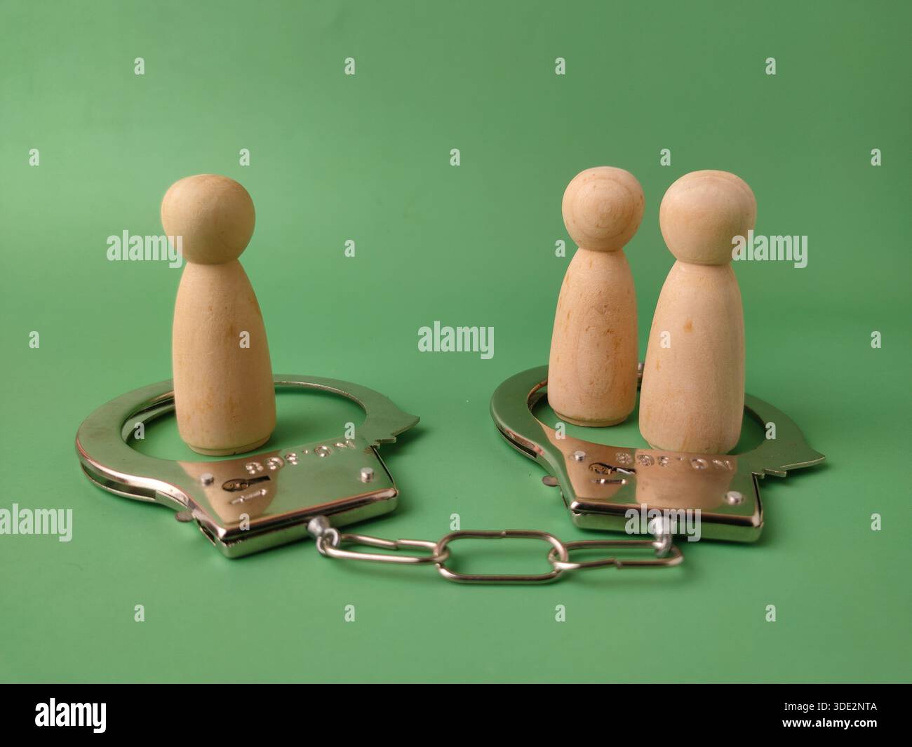 Die Handschellen symbolisieren Autorität, Kontrolle und die Folgen von Fehlverhalten, während die beiden getrennten Holzfiguren Einzelpersonen oder vielleicht ein Paar repräsentieren, das sich diesen Themen einzeln oder gemeinsam stellt. Stockfoto