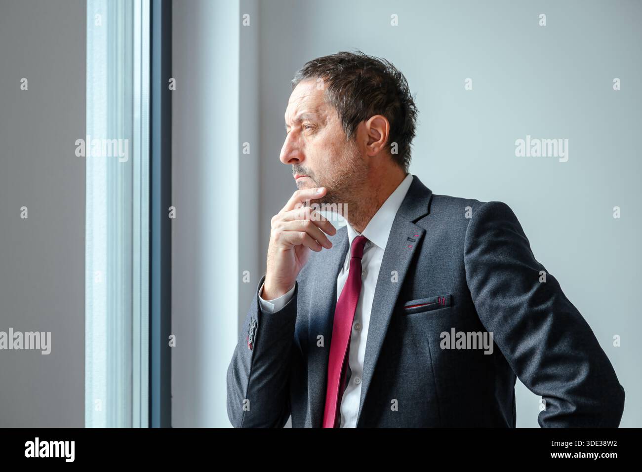 Müder und besorgter Geschäftsmann, der am Fenster des Büros steht, in Gedanken verloren. Selektiver Fokus. Stockfoto