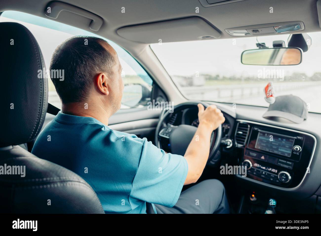 Ein Weißer mittleren Alters mit kurzen Haaren fährt ein Auto auf der Autobahn. Er wirkt konzentriert und entspannt und genießt die Reise. Stockfoto