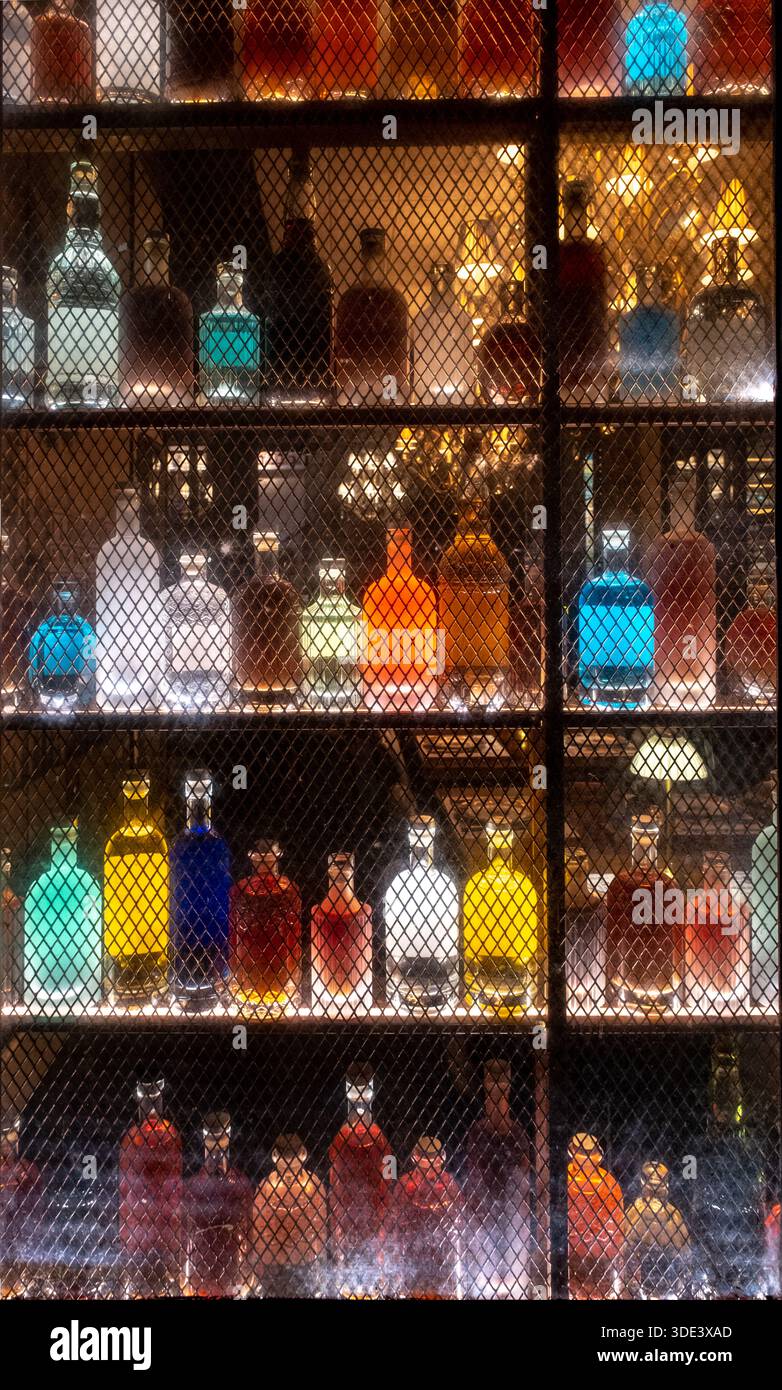 Farbenfrohe Spirituosenflaschen auf beleuchteten Barregalen mit Neonlichtern hinter einem abgeschirmten Fenster Stockfoto