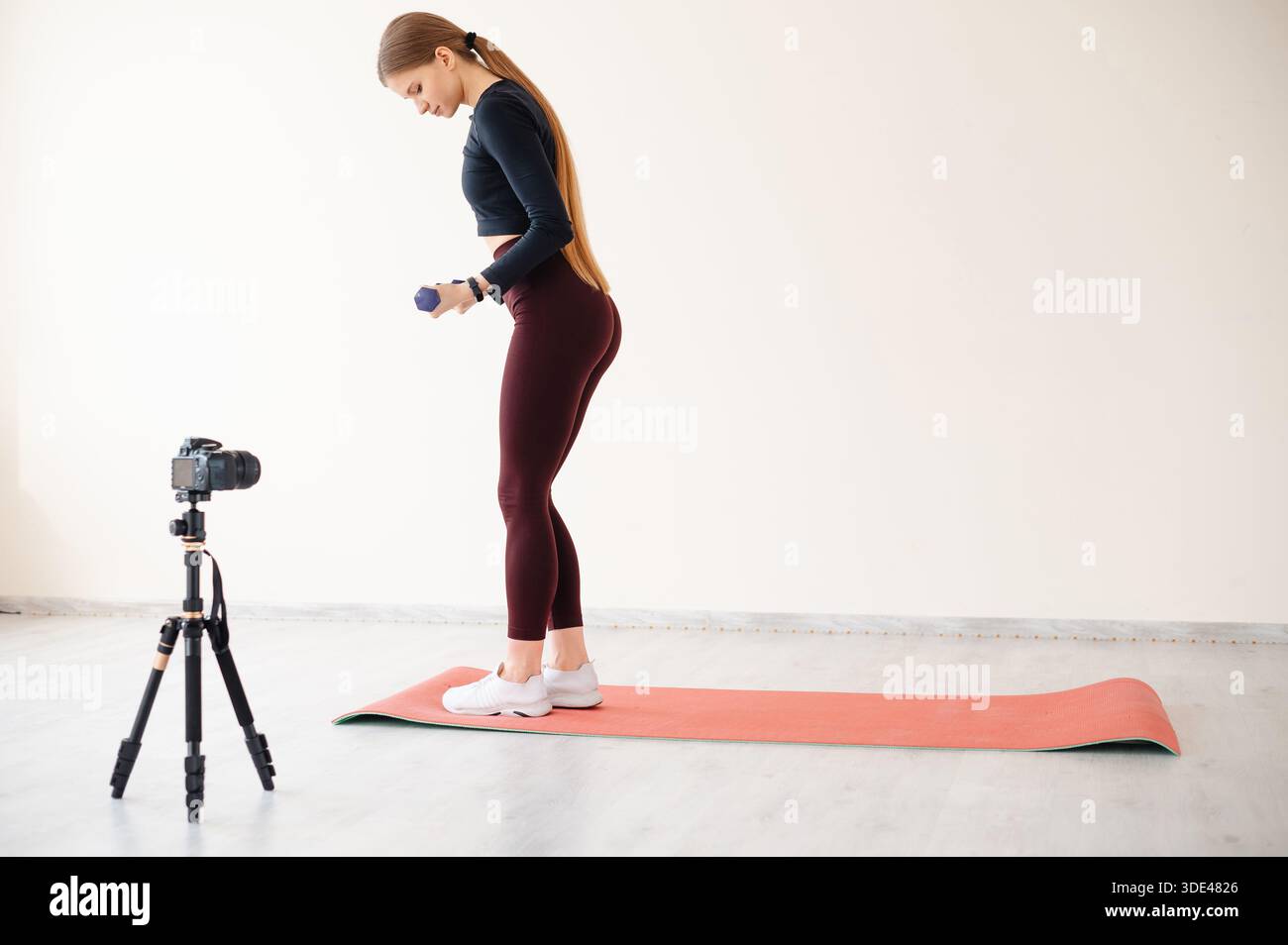 Frau filmt ihr Heimtraining mit Kurzhanteln und einer Kamera auf einem Stativ Stockfoto