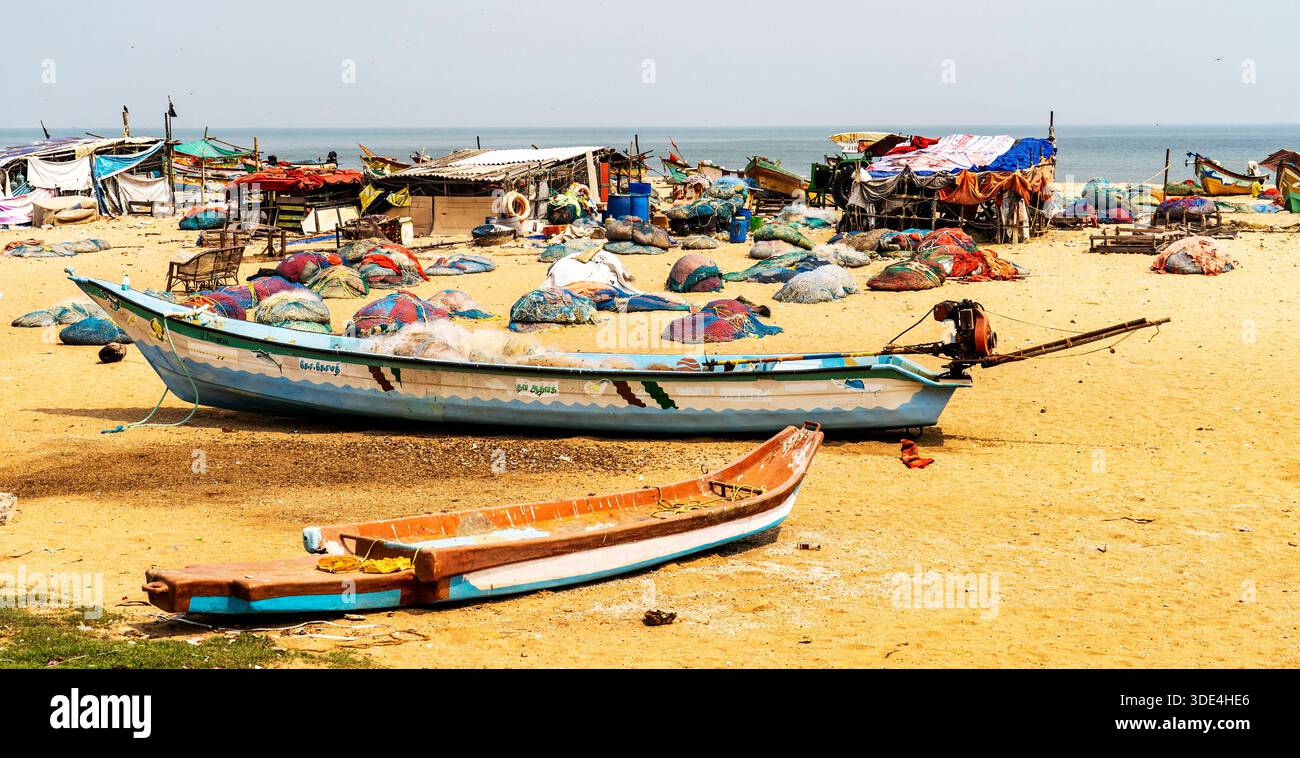 Fischerboote und Netze an einem Sandstrand mit Hütten im Hintergrund. Stockfoto