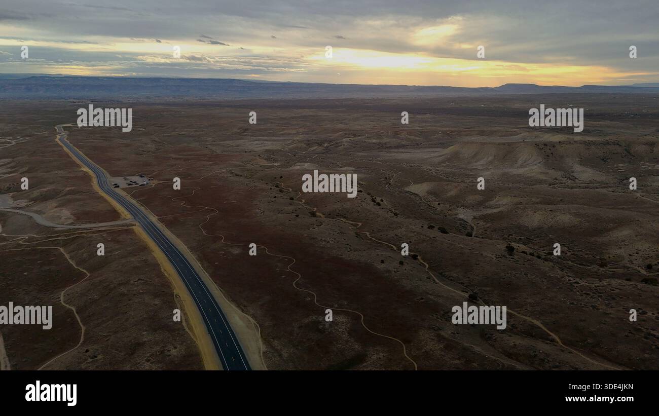 Aus der Vogelperspektive einer langen, geraden Straße durchquert die trockene Landschaft unter einem weiten Himmel, der von sanften Morgentönen getönt ist, Fruita, Colorado, United Stat Stockfoto