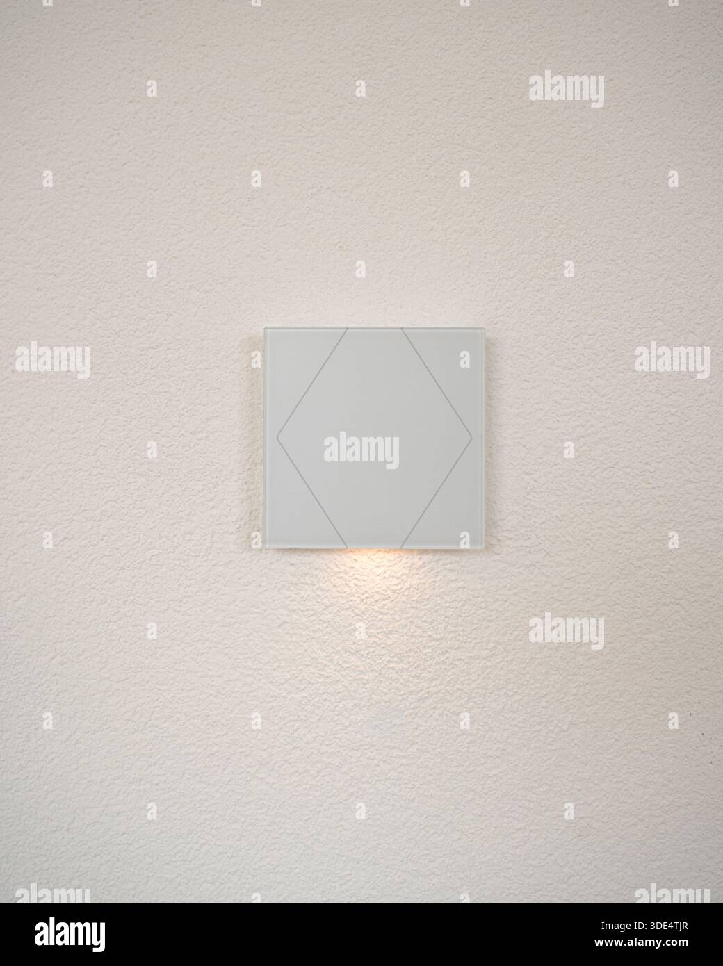 Einfache Wandleuchte leuchtet sanft auf einer strukturierten weißen Wand. Das moderne Design und die warme Beleuchtung machen es für Innenarchitektur, Wohnkomfort und Stockfoto