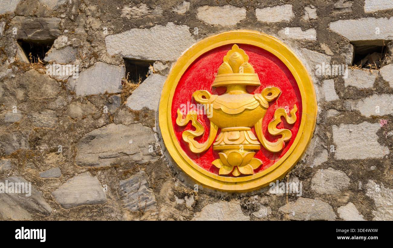 Ein kreisförmiges Relief mit einer stilisierten Vase auf rotem Hintergrund, umgeben von einem gelben Rahmen auf einer Steinmauer. Stockfoto