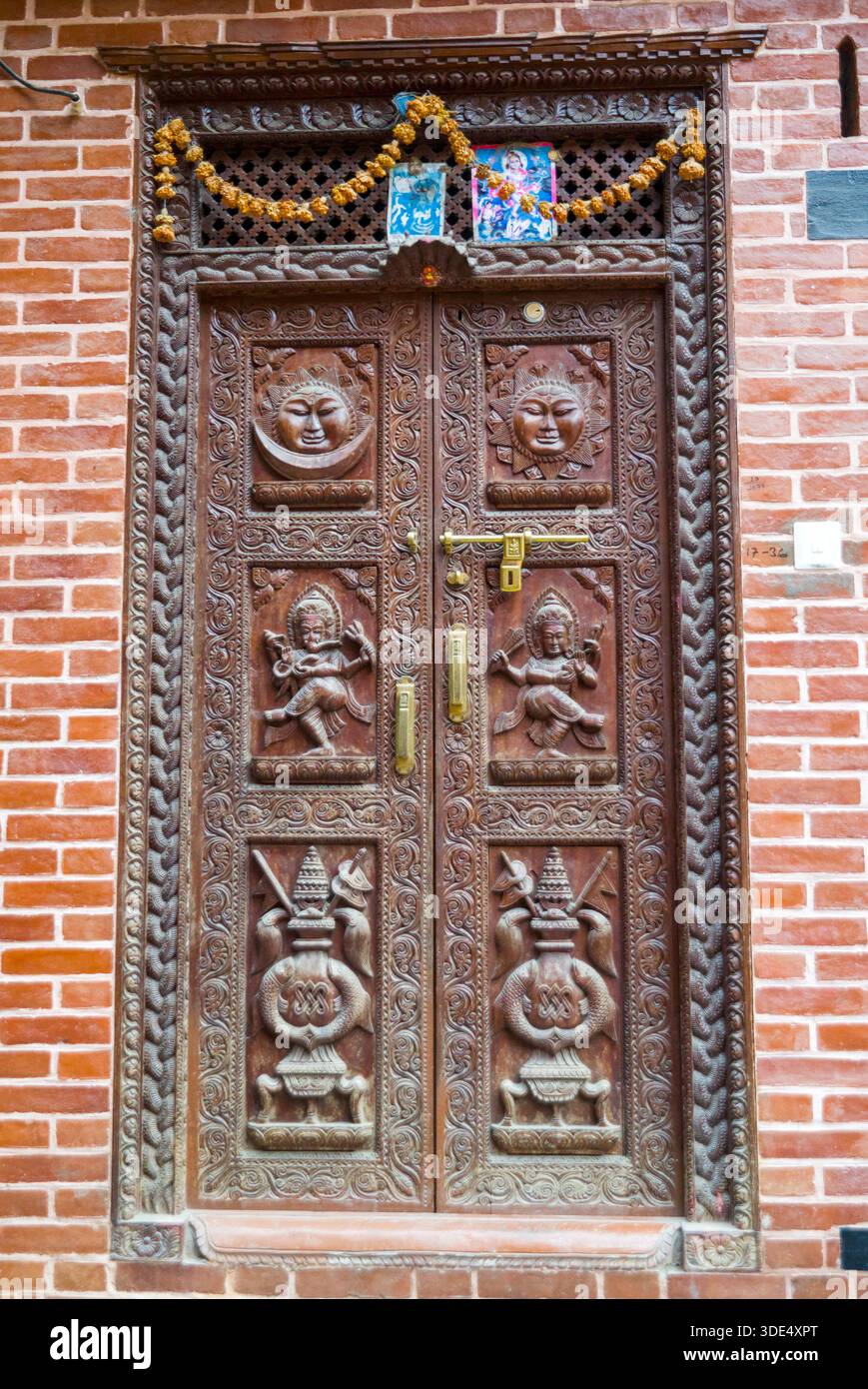 Eine künstlerisch geschnitzte traditionelle Holztür mit religiösen Motiven und dekorativen Metallbeschlägen, die spirituelles und handwerkliches Erbe zeigen. Stockfoto