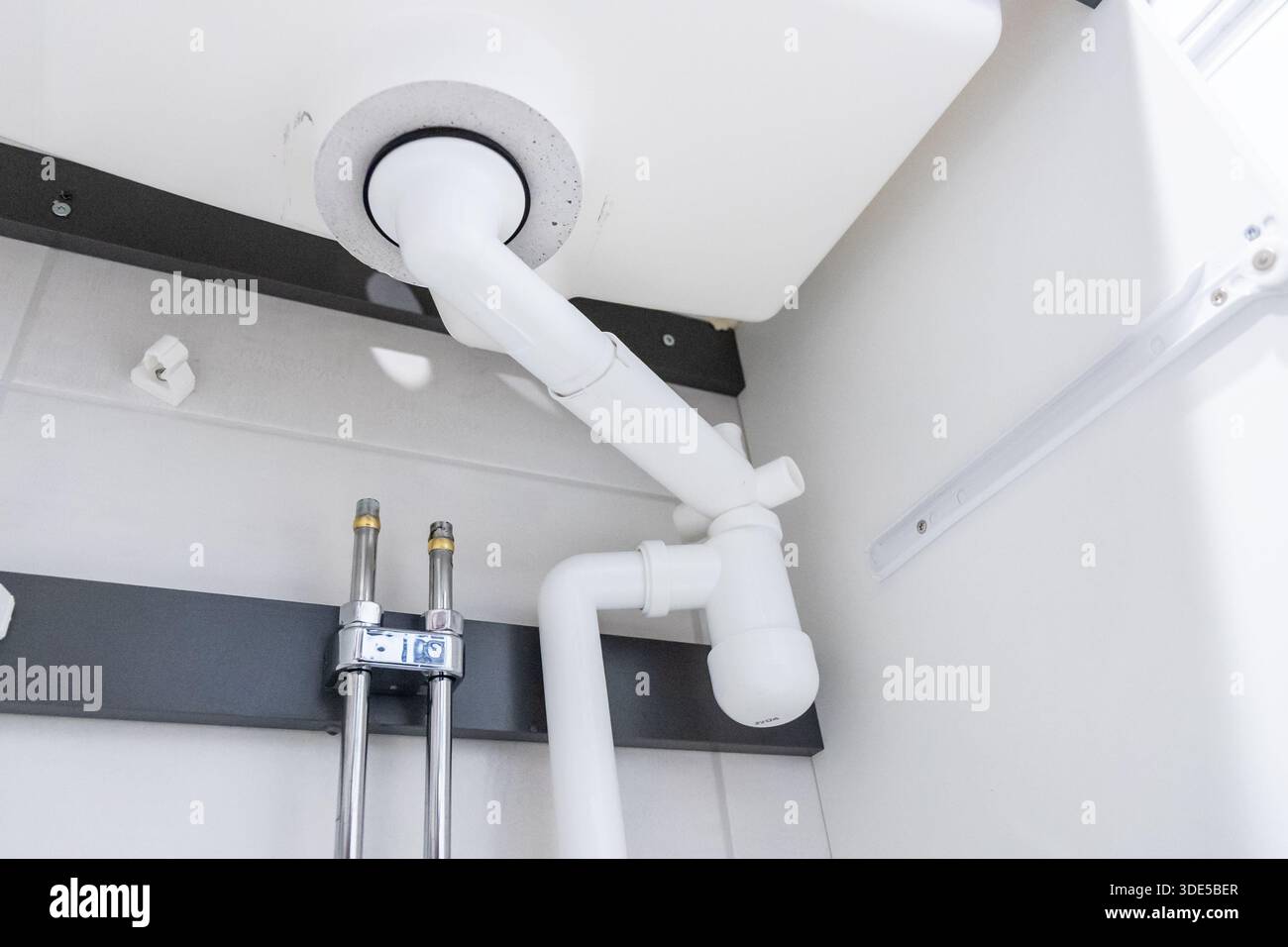 Sanitäranlage unter einem Waschbecken mit P-Falle und Hansgrohe SBOX-System für einen herausziehbaren Wasserhahn. Moderne Installation mit organisierten Rohrleitungen und f Stockfoto