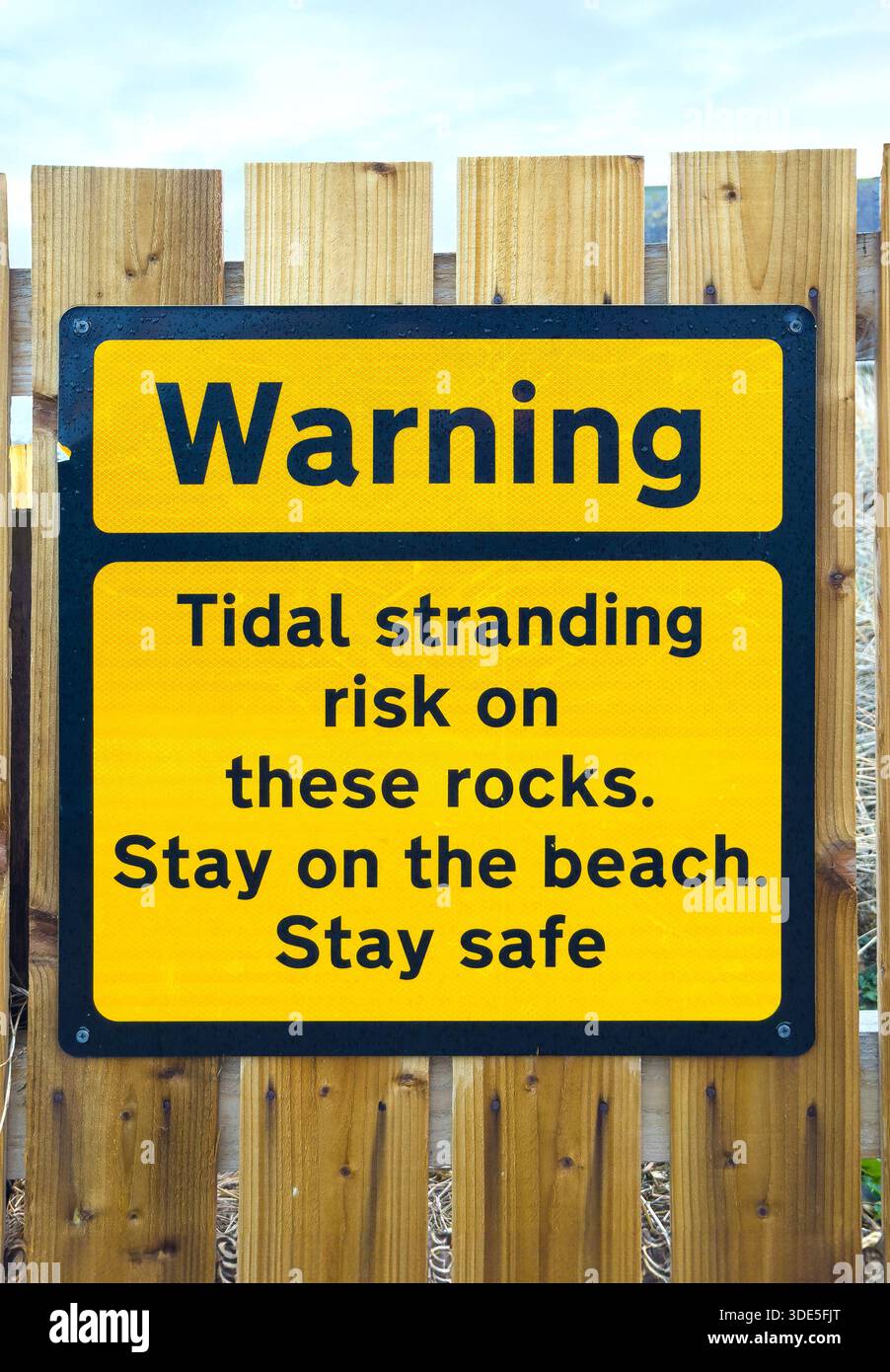 Hellgelbes Warnschild, das die Strandbesucher auf das Risiko von Gezeiten auf den Felsen aufmerksam macht und ihnen empfiehlt, aus Sicherheitsgründen am Strand zu bleiben cresswell Stockfoto