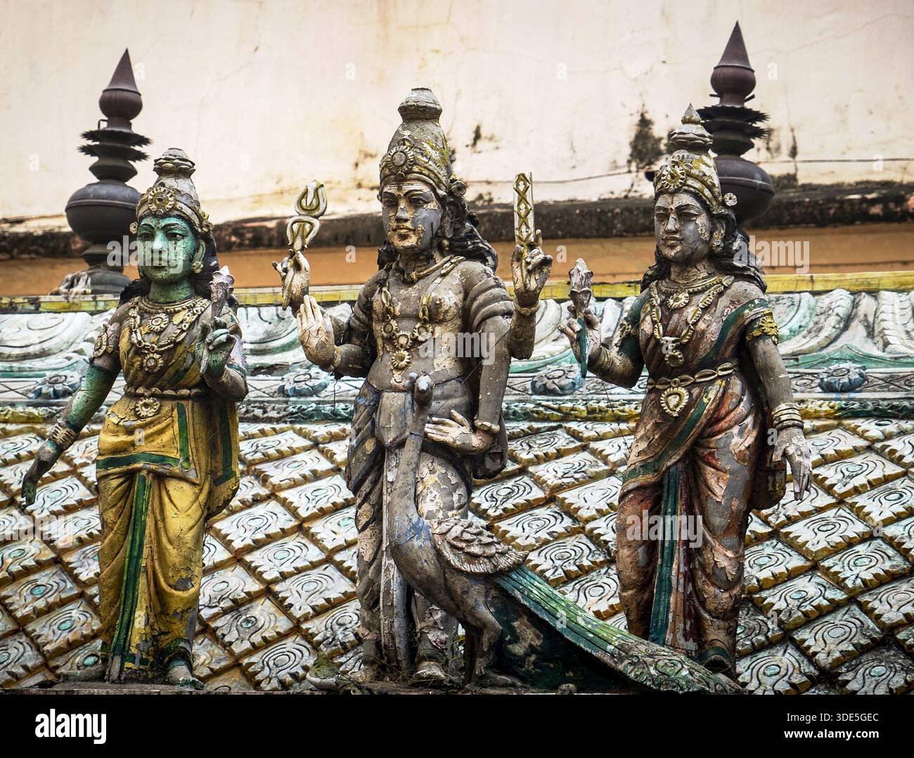 Drei aufwendig geschnitzte hinduistische Gottheiten an einer Tempelfassade mit traditioneller Kleidung und symbolischen Gesten, mit verwittertem, historischem Aussehen. Stockfoto