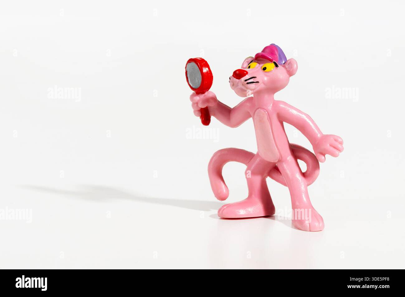 Pinkfarbene Panther-Zeichentrickfigur mit einer kleinen roten Lupe auf weißem Hintergrund Stockfoto
