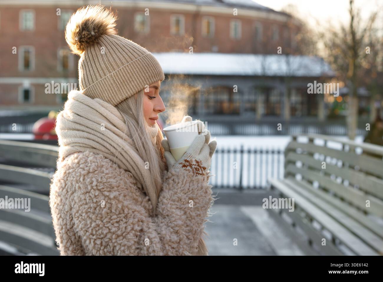 Zufriedene Frau hält im Winter draußen eine Tasse heißen Tee oder Kaffee, heißer Dampf kommt aus der Tasse Stockfoto