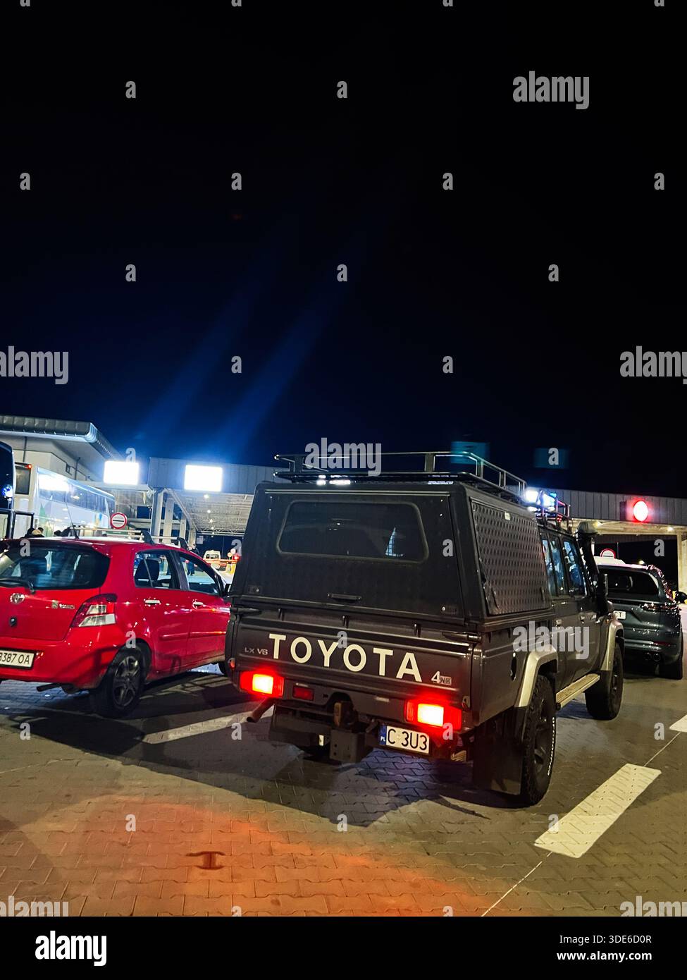 Nyzhankovychi, Ukraine - 03. November 2025: Eine Nachtszene, die einen robusten Toyota Land Cruiser LX V6 neben einem roten Auto auf einem belebten Parkplatz zeigt. Stockfoto