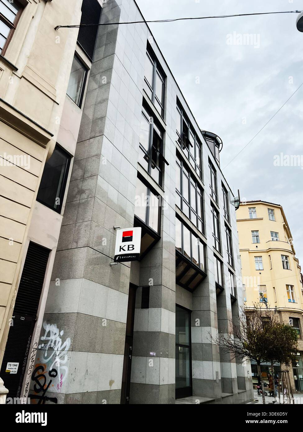 Brünn, Tschechische Republik - 29. November 2025: Städtische Brünner Straßenszene mit einem modernen Glasgebäude, einer grauen Steinfassade und einem KB-Bankschild unter einem Clo Stockfoto