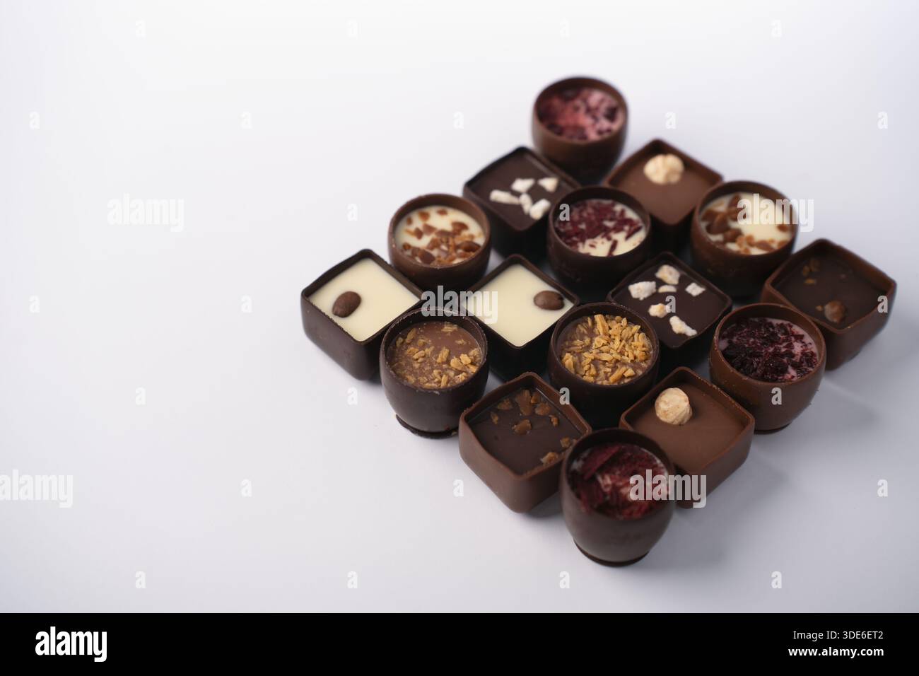Verschiedene handgemachte Schokoladenpralinen und Trüffel auf einer sauberen weißen Tischplatte in minimalistischer Studioatmosphäre, glänzende dunkle und weiße Ganache wi Stockfoto