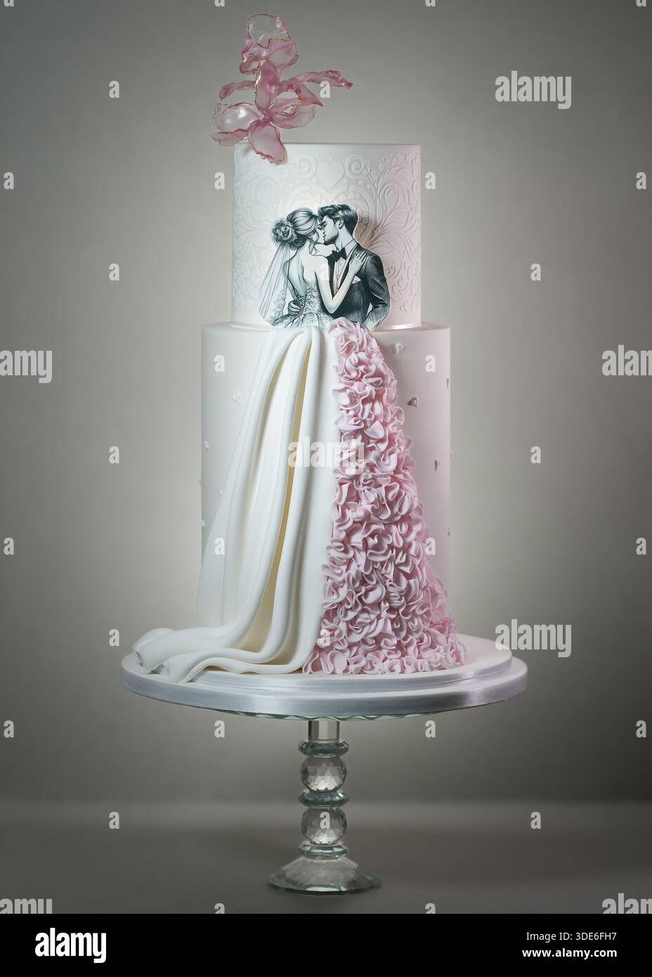 Hohe, luxuriöse Hochzeitstorte mit romantischer Silhouette, komplizierten Damastmustern, rosa Waffelpapierblumen und einem strukturierten Rüschenzug Stockfoto