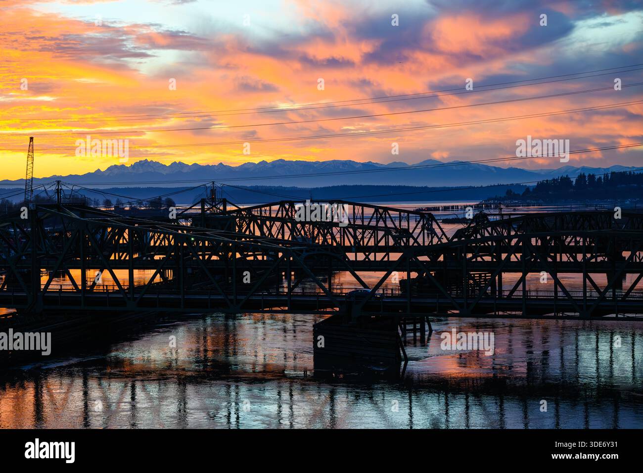 Farbenfroher Sonnenuntergang über den Olympischen Bergen und Straßen- und Eisenbahnbrücken über Steamboat Slough Stockfoto