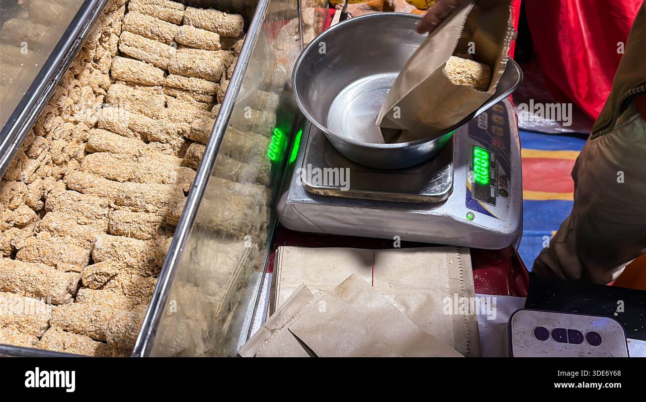 Traditionelle indische Süßigkeiten Sesambrüchig werden am Marktstand für den Einzelhandel gewogen Stockfoto