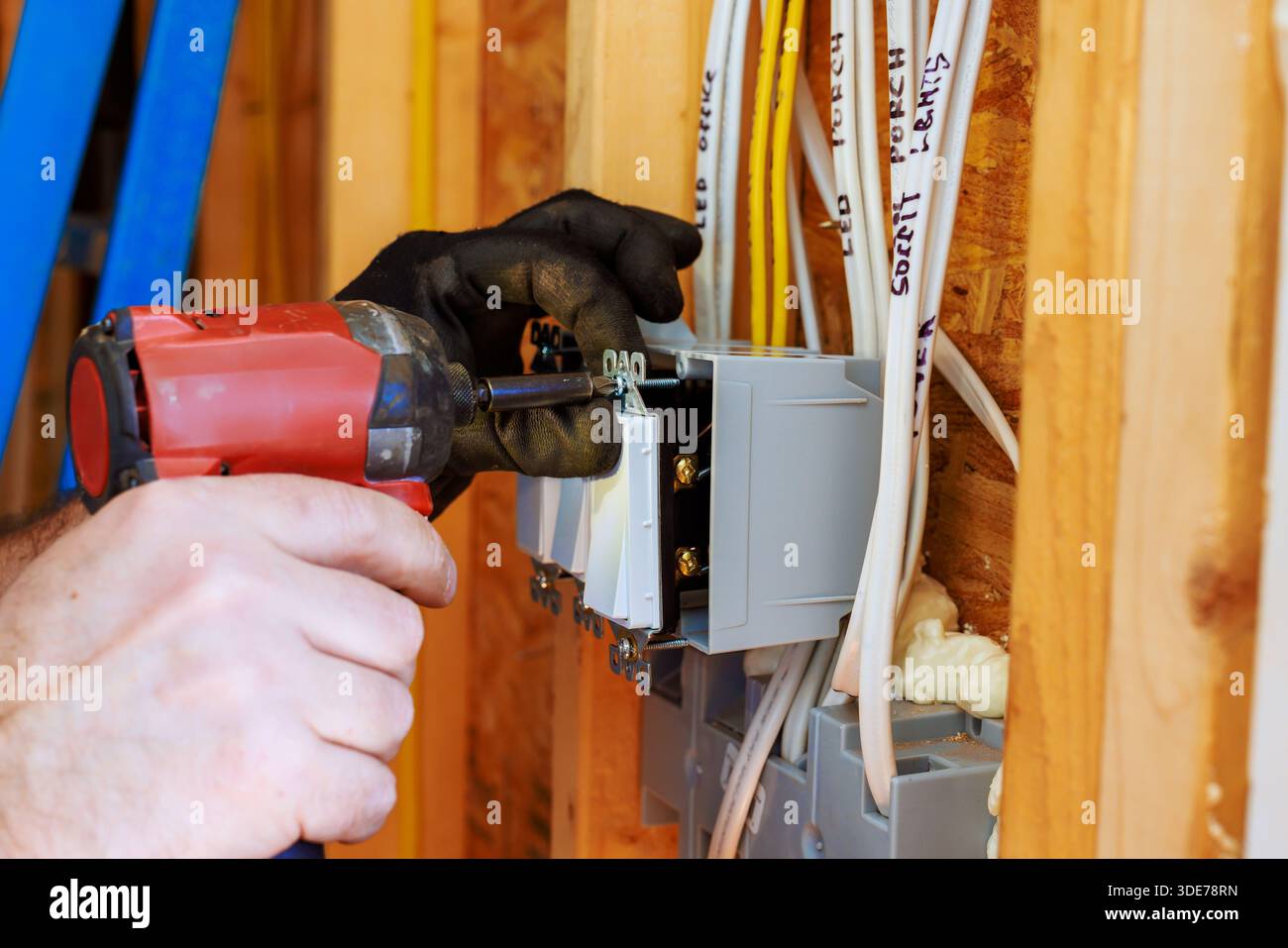 Ein Elektriker verwendet ein Elektrowerkzeug, um Leistungsschalter in der Wand des neu errichteten Hauses zu installieren Stockfoto