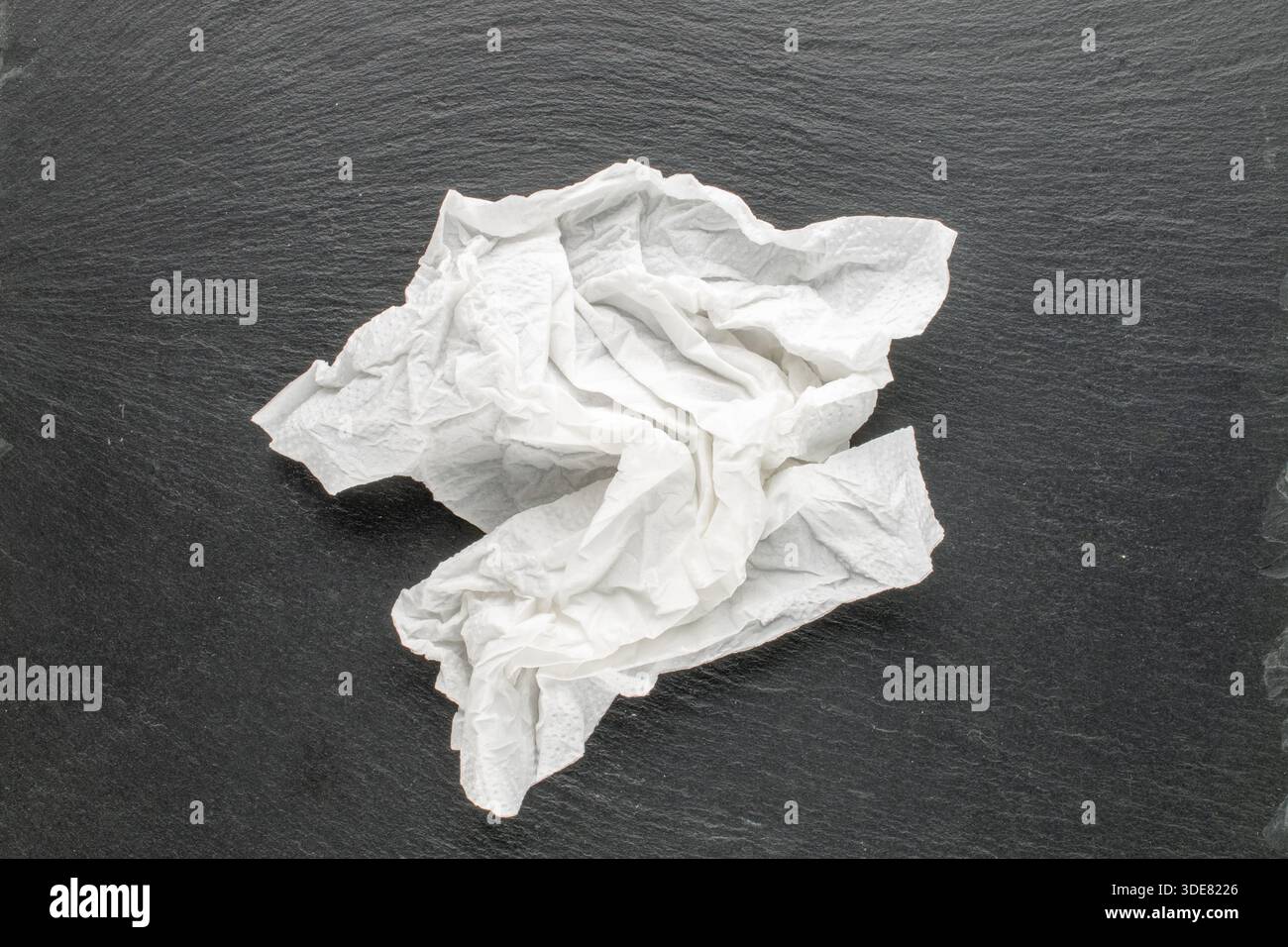 Weiße zerknitterte Papierserviette auf Schieferstein, Makro, Draufsicht. Stockfoto