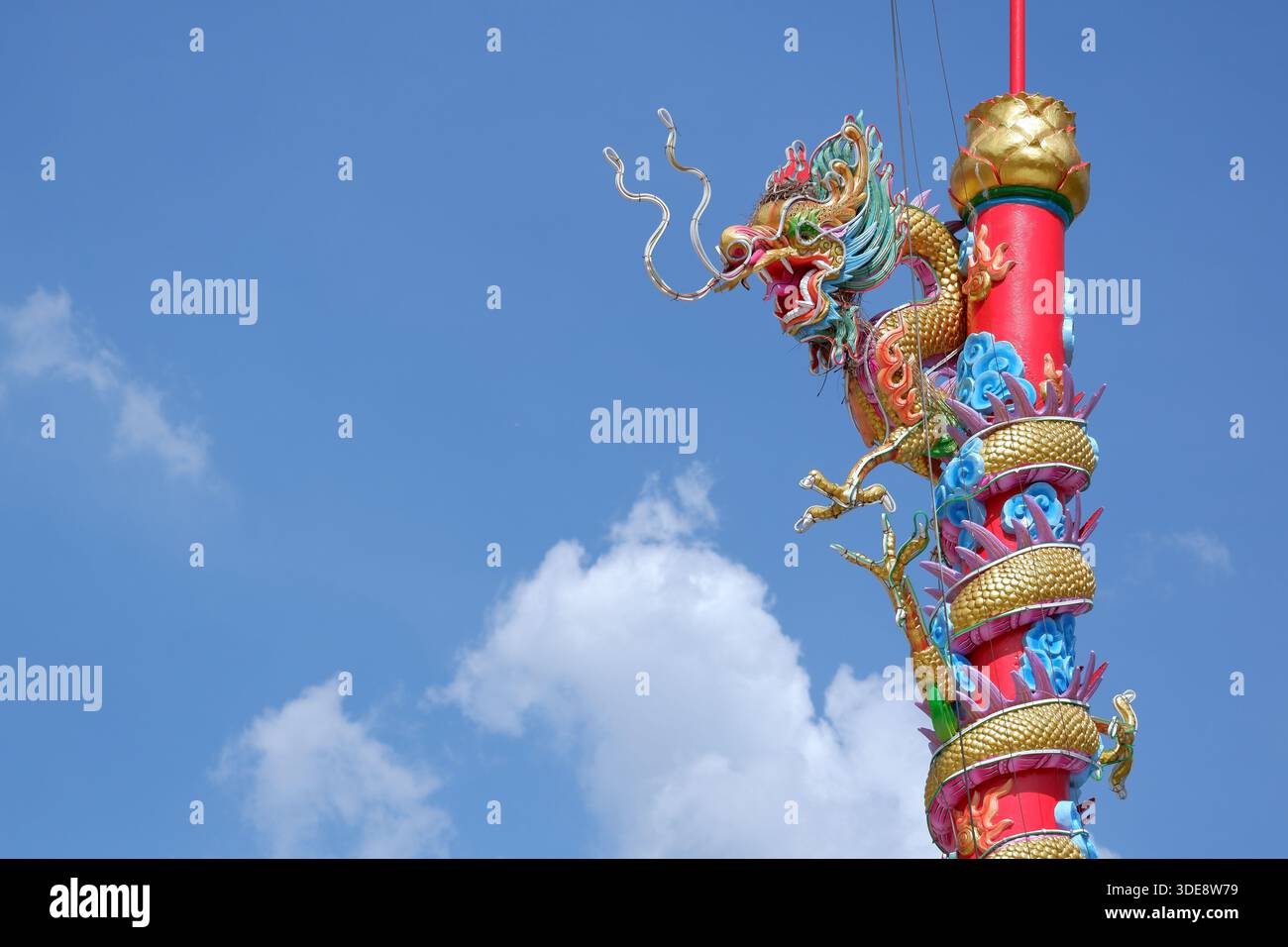 Ein lebendiges chinesisches Drachendenkmal dreht sich um einen hohen roten Stab, der mit einer Hängelampe gekrönt ist, und steht vor weichen Wolken und blauem Himmel. Stockfoto