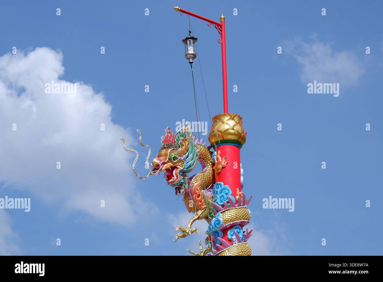 Ein mehrfarbiges chinesisches Drachendenkmal dreht sich um einen hohen roten Stab, der mit einer Hängelampe gekrönt ist, und steht vor weichen Wolken und blauem Himmel. Stockfoto