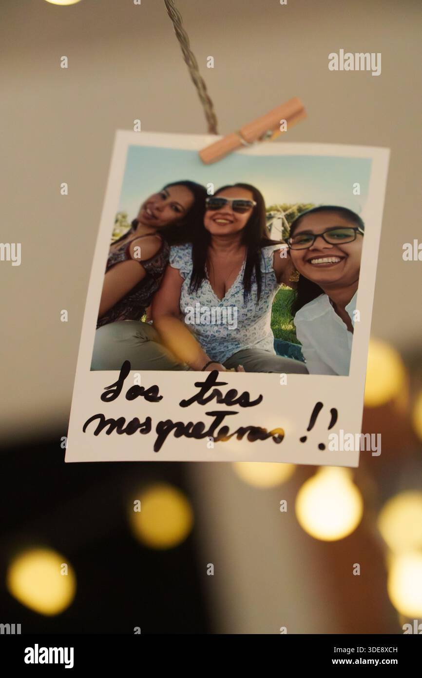 Ein Foto von drei Frauen mit einer Notiz, auf der steht "Sao te musquem!". Das Foto hängt an einer Schnur Stockfoto