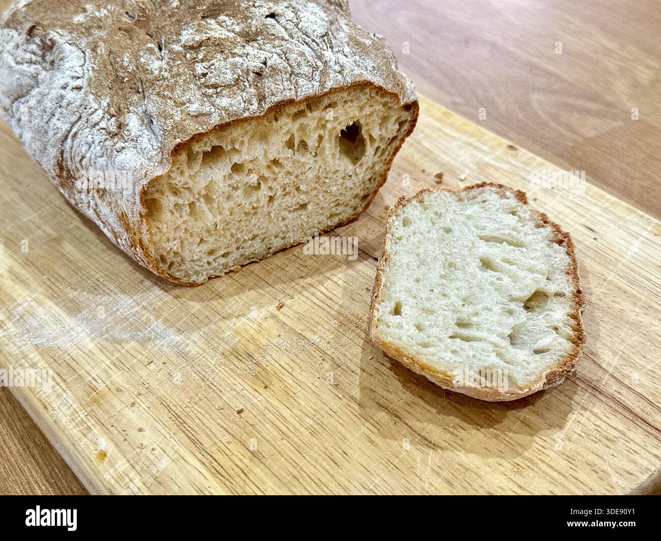 Ein Stück frisches, hausgemachtes, knuspriges Sauerteigbrot mit einer Scheibe, nachdem es auf einem Brett geschnitten wurde Stockfoto