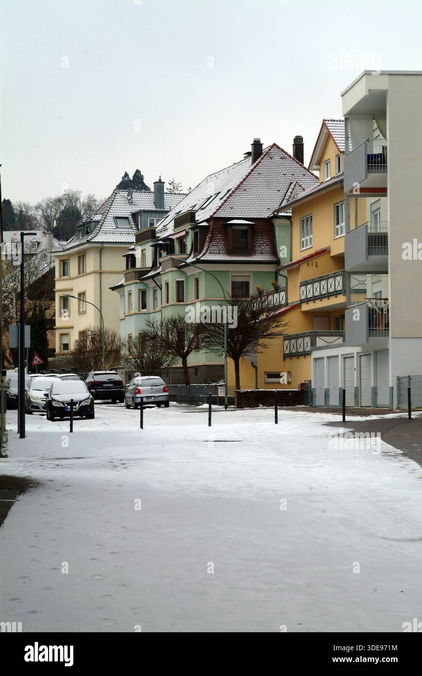 Bezaubernde, schneebedeckte Reihe von bunten Häusern, schneebedeckte Dächer, ordentlich geparkte Autos, schmale Straße, die durch eine gemütliche Wohngegend Keukenhof führt, Stockfoto