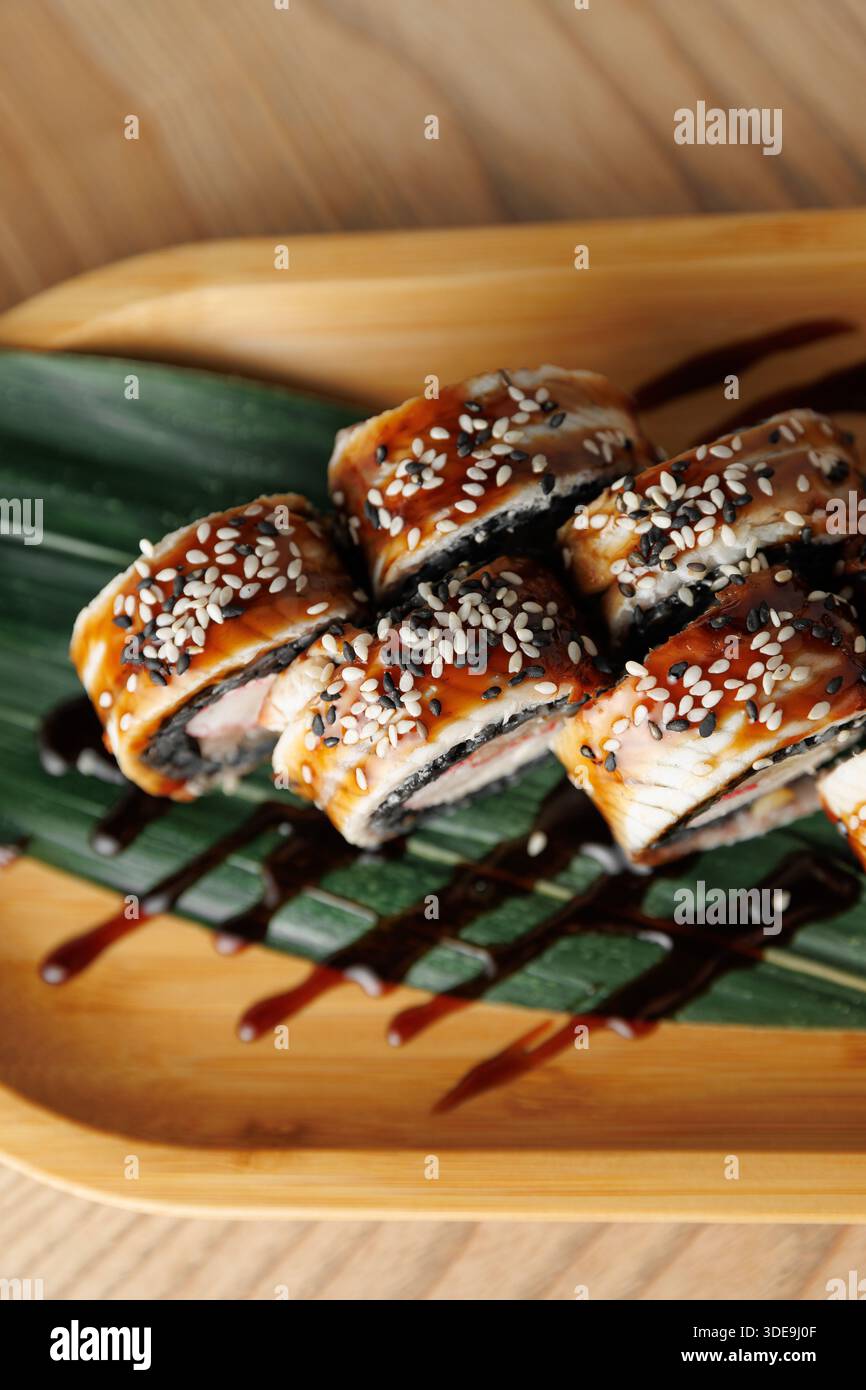 Sushi-Brötchen mit Aal und Sesamsamen sind auf einem Bambusteller angeordnet. Eine würzige Sauce wird über die Brötchen getränkt, die Sie genießen können Stockfoto