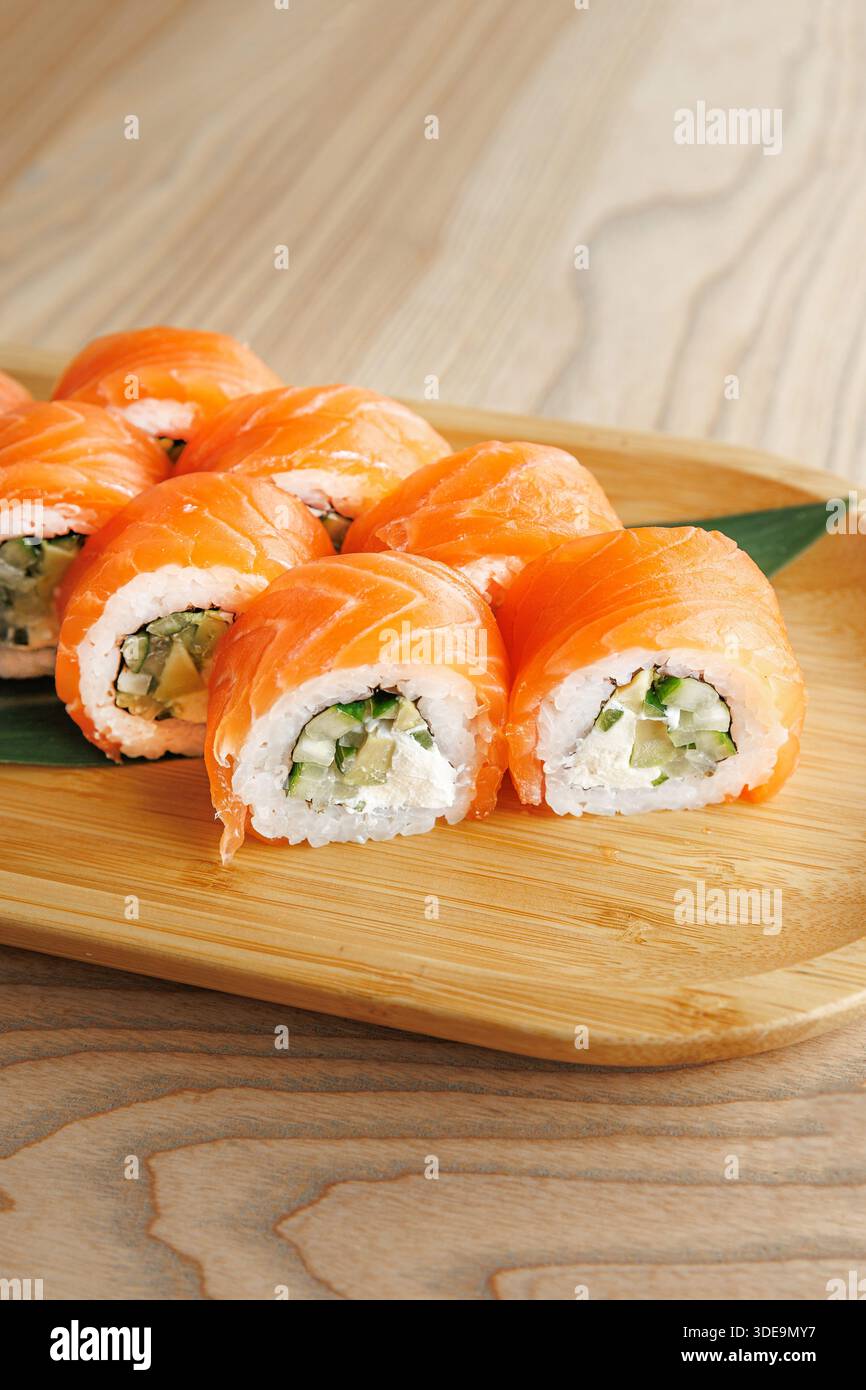 Auf einem Holzbrett werden frische Sushi-Brötchen mit Lachs und Gurke präsentiert. Dieses Gericht zeigt die Kunst der japanischen Küche, bereit zum Mittagessen Stockfoto