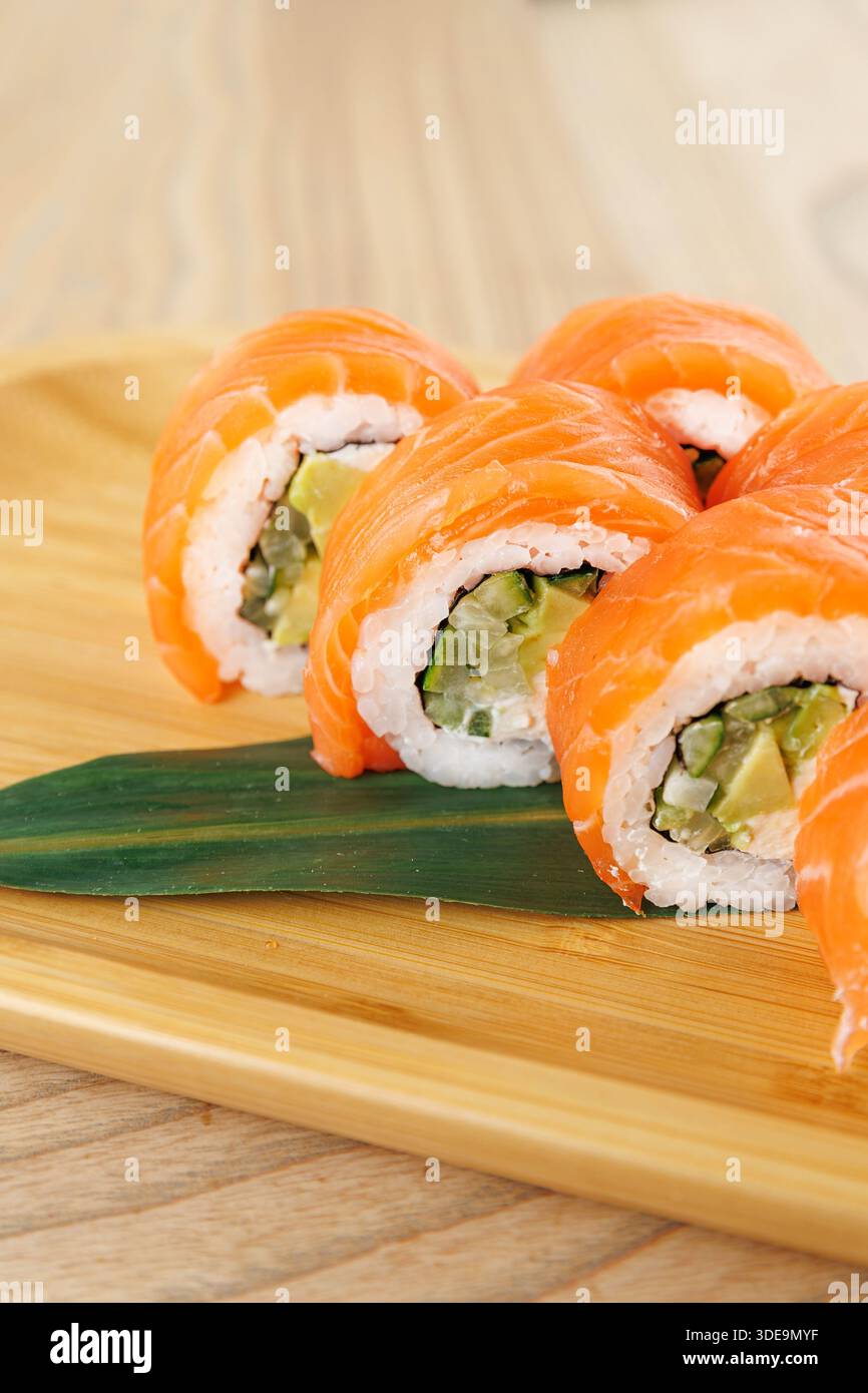 Frisch zubereitete Sushi-Brötchen gefüllt mit Avocado und Gemüse sind ordentlich auf einem Holzteller angeordnet, in lebendigen Farben. Dieses Gericht ist bereit für en Stockfoto