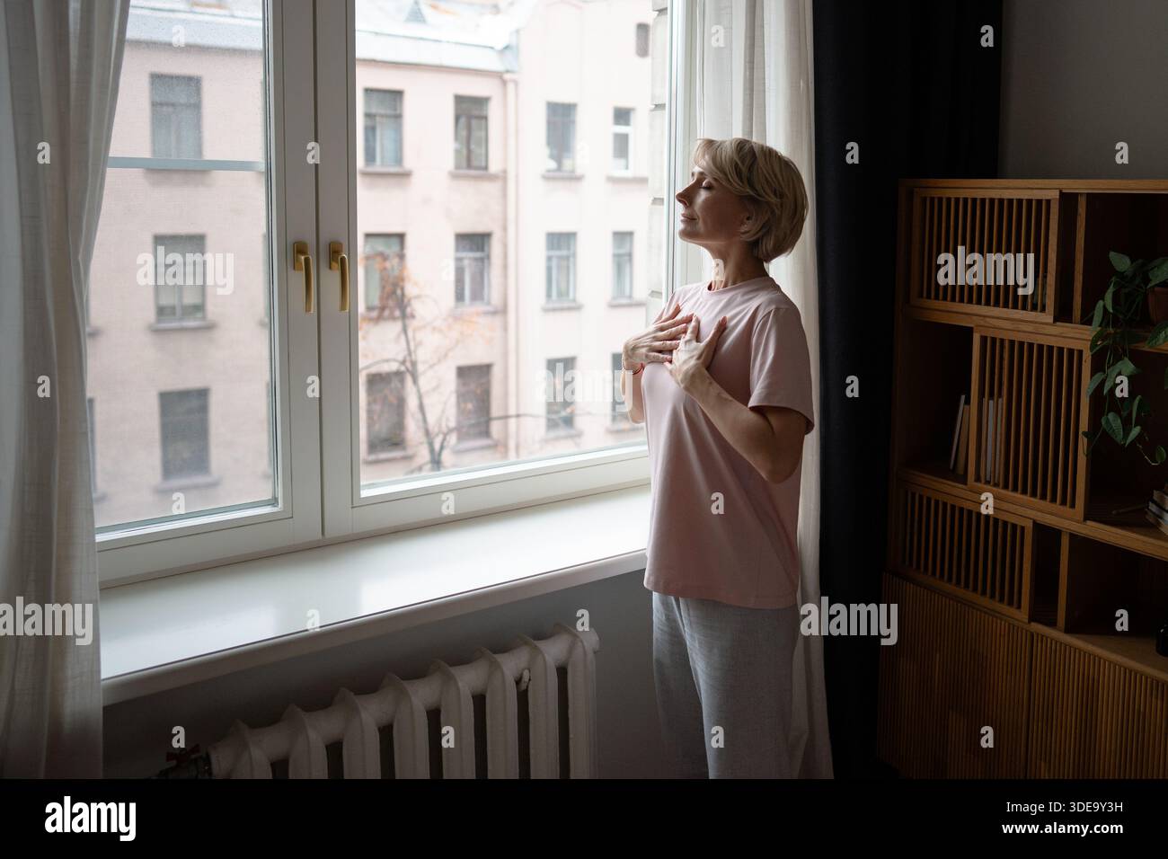 Lächelnde Frau mit geschlossenen Augen, die Atemübungen übt, tief einatmet mit den Händen auf der Brust. Stockfoto