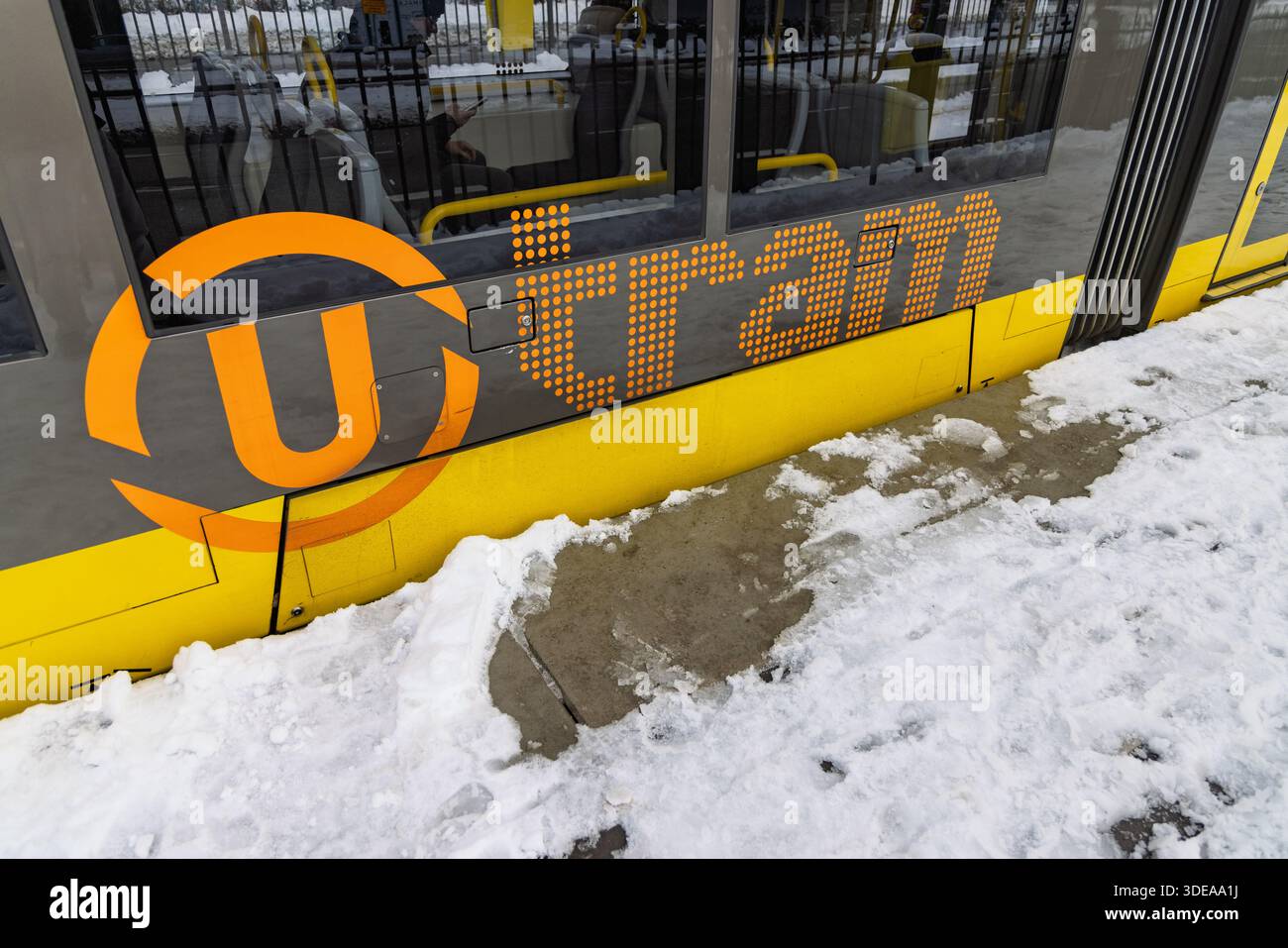 Detailaufnahme der gelben Seitenverkleidung einer Straßenbahn in Utrecht mit dem orangefarbenen U-Tram-Logo, das neben einem schneebedeckten Bahnsteig geparkt ist. Utrecht Ne Stockfoto