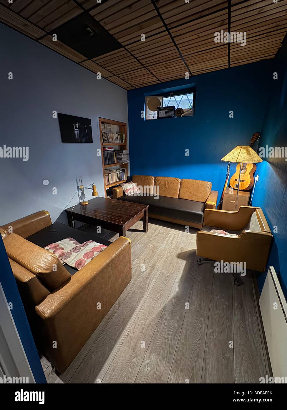 Gemütliche Leselounge mit Sesseln, Gitarre, Bücherregal und warmer Beleuchtung in stilvoller Einrichtung - Smartphone-aufgenommenes Stockfoto