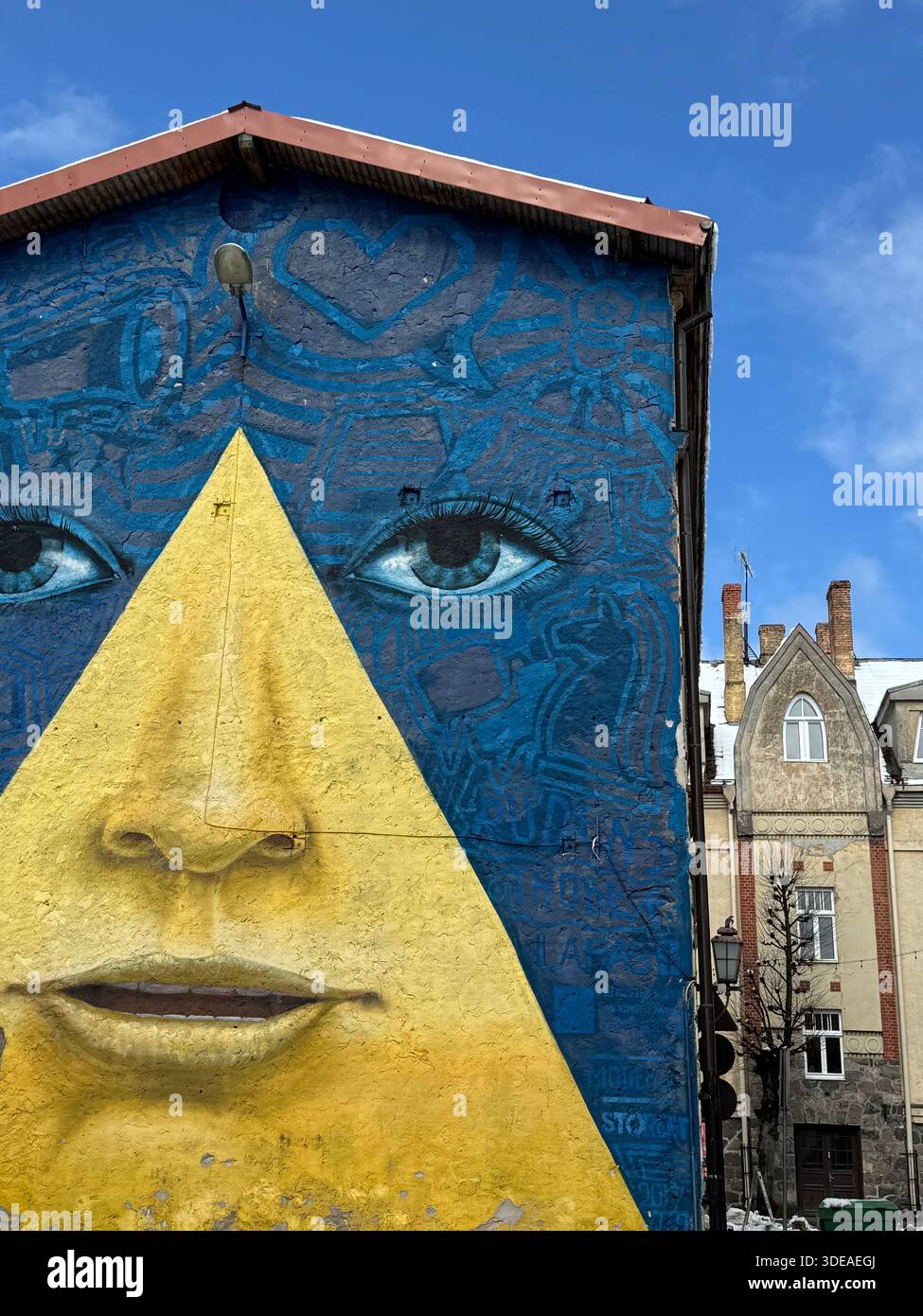 Farbenfrohes Wandgemälde mit stilisiertem menschlichem Gesicht auf der Gebäudefassade, das geometrische und expressive Elemente kombiniert - Smartphone-aufgenommenes Stockfoto